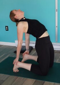 Dr. chloe demonstrating  the medium difficulty version of camel pose which is with your toes tucked under to elevate your heels.  She is on her knees, extending through her hips and thoracic spine